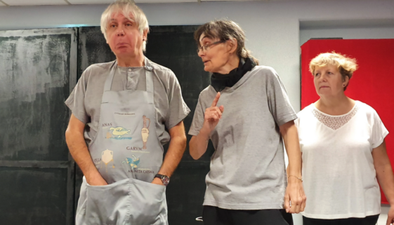 Répétition de l'atelier Théâtre Forum de PasSages : une participante interpelle un homme en tablier, une autre observe la scène.
