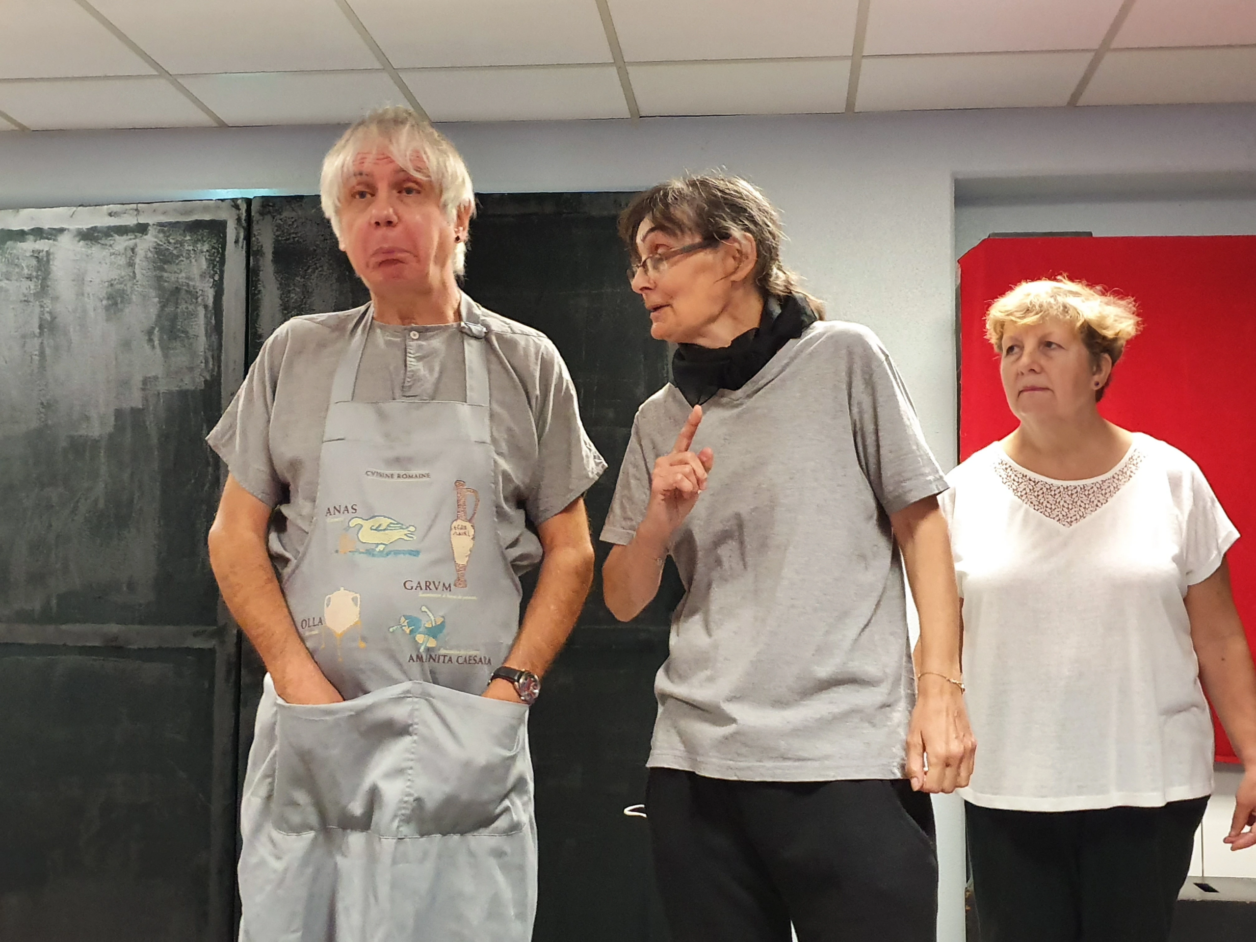 Répétition de l'atelier Théâtre Forum de PasSages : une participante interpelle un homme en tablier, une autre observe la scène.